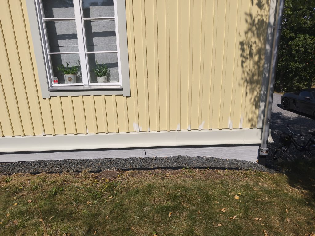 Aken kollasel voodrilaual ja selle all valmis sokkel