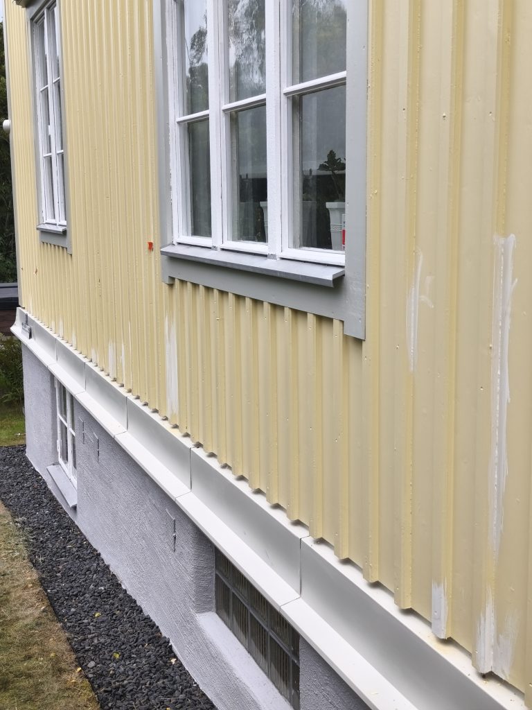 Kollane voodrilaud ja hele viimistletud sokkel maja küljel